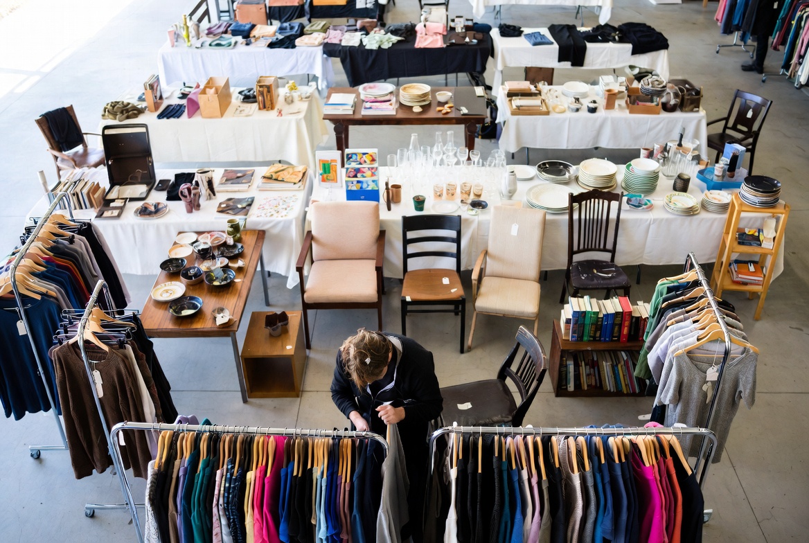Stand de vide-grenier bien organisé avec vêtements sur portants, meubles et objets bien présentés